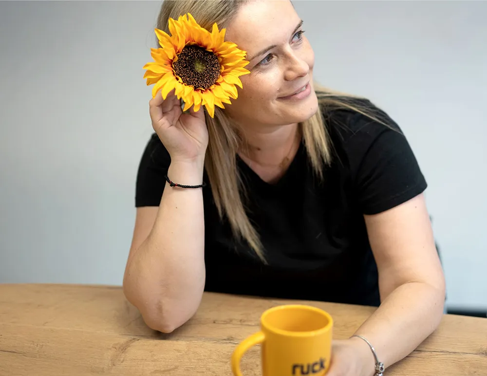 Anca sitzt an einem Tisch mit einer Sonnenblume im Haar.
