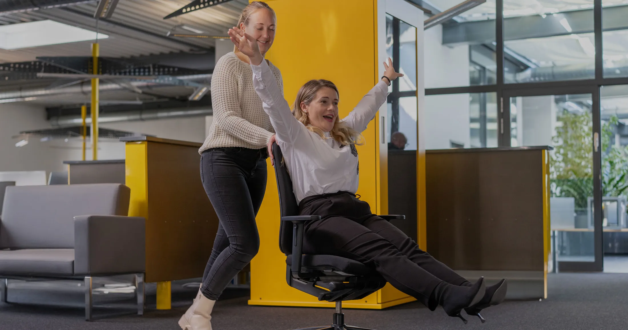 Anca wird auf einem Bürostuhl durchs Büro geschoben.