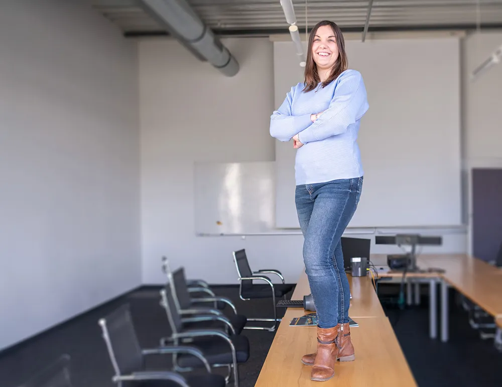 Miriam steht auf einem Tisch in einem Besprechungsraum und berichtet über ihren Arbeitsalltag.