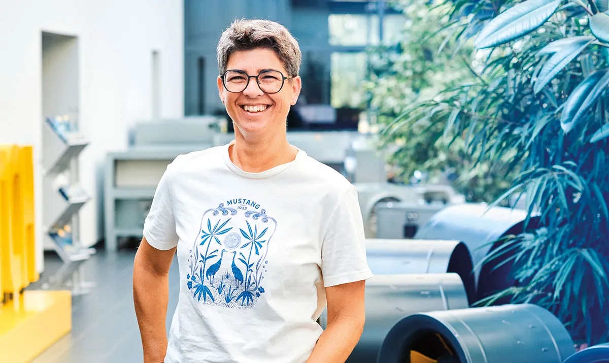 Mitarbeiterin von ruck in der Produktionsumgebung mit Ventilatorbauteilen im Hintergrund als Symbol für vorausschauendes Handeln und Entwicklung.